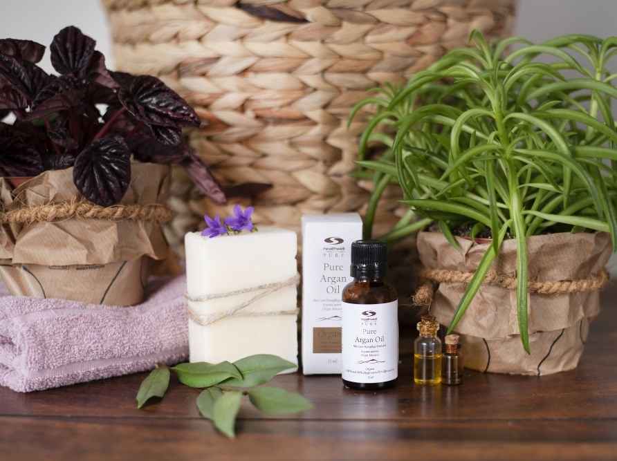 pure argan oil sitting with the carton, plants and a soap in front of a basket.