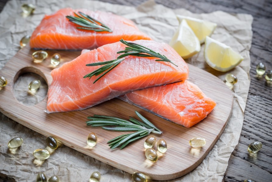 Three salmon fillets on a cutting board with omega-3 capsules and lemon wedges. Three salmon fillets on a cutting board with omega-3 capsules and lemon wedges.